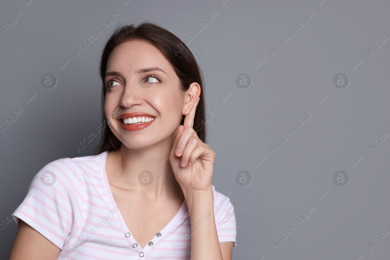 Photo of Woman showing hand to ear gesture on grey background, space for text