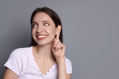 Photo of Woman showing hand to ear gesture on grey background, space for text