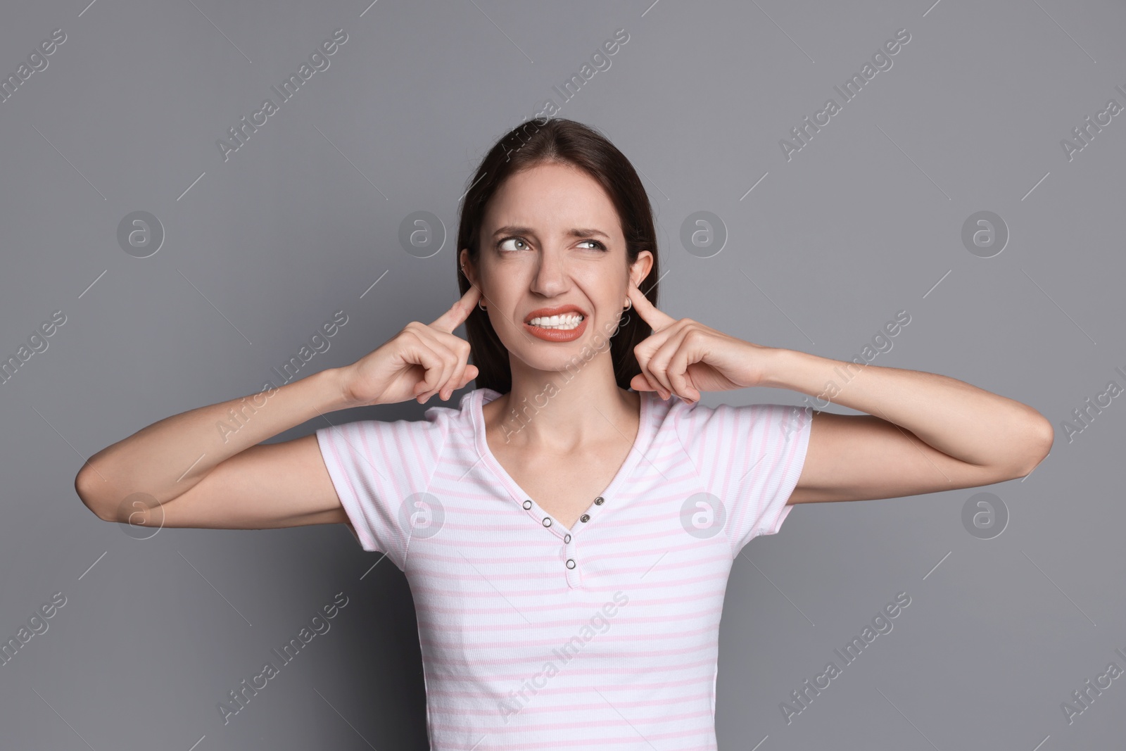 Photo of Woman covering her ears with fingers on grey background