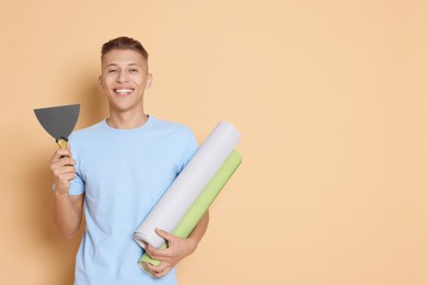 Photo of Young decorator with putty knife and rolls of wallpaper on beige background, space for text