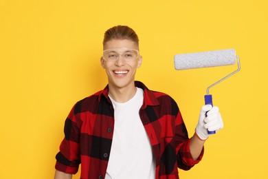 Photo of Portrait of young decorator with paint roller on orange background