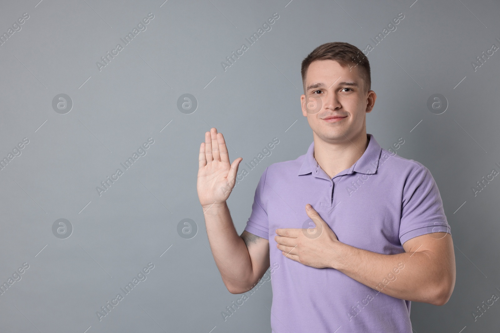 Photo of Man making promise with raised hand on grey background, space for text. Oath gesture