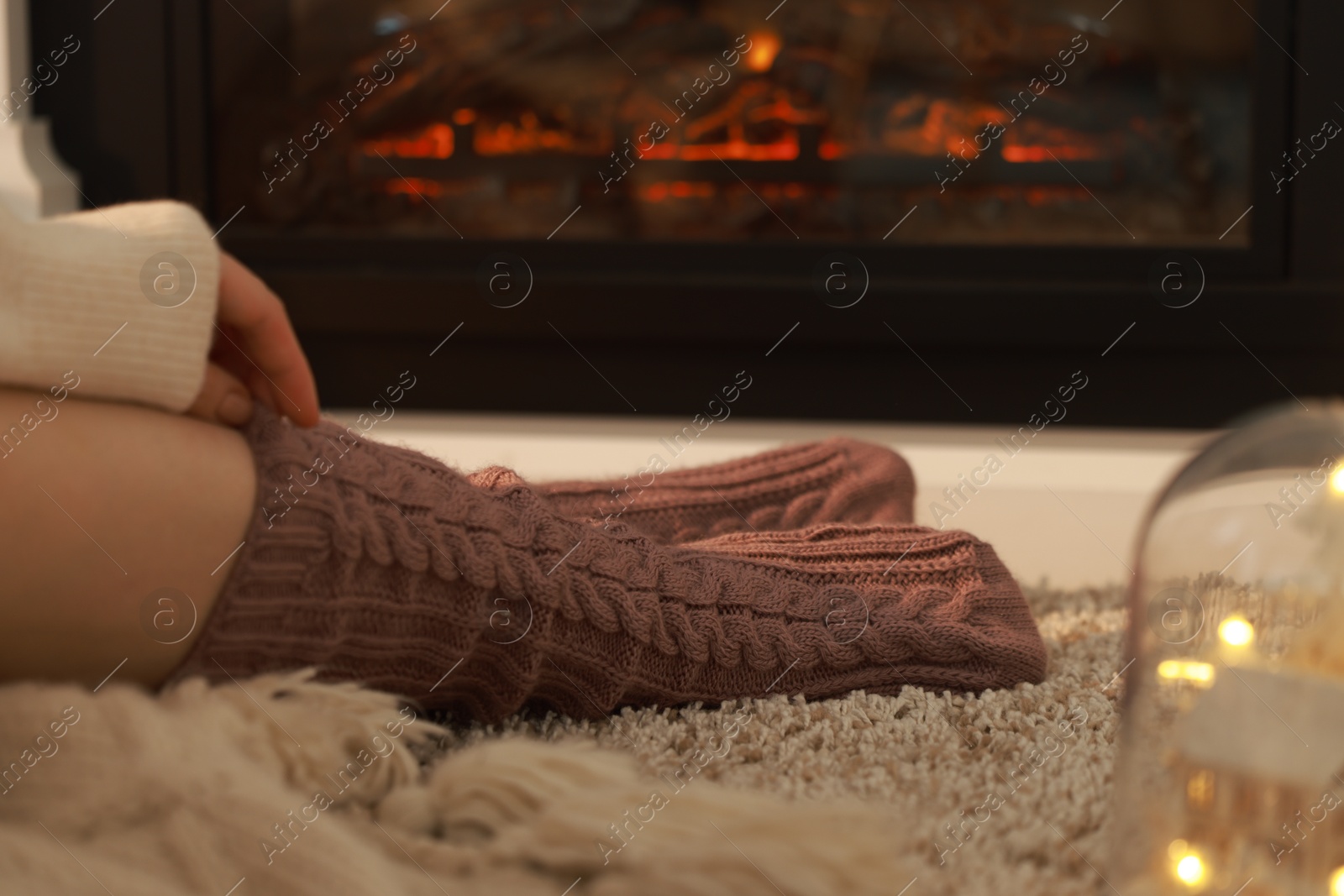 Photo of Woman in knitted socks resting near fireplace at home, closeup