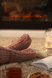 Photo of Woman in knitted socks resting near fireplace at home, closeup