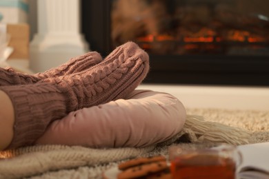 Photo of Woman in knitted socks resting near fireplace at home, closeup