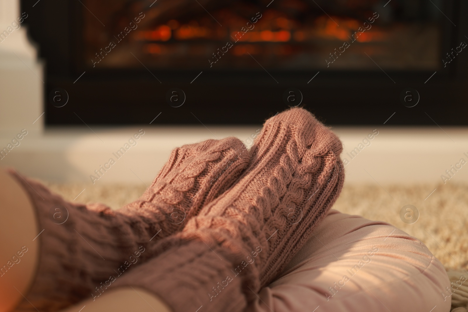 Photo of Woman in knitted socks resting near fireplace at home, closeup