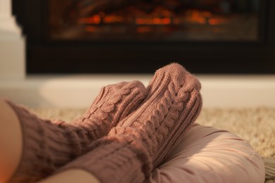 Woman in knitted socks resting near fireplace at home, closeup