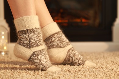 Photo of Woman in warm socks resting near fireplace at home, closeup