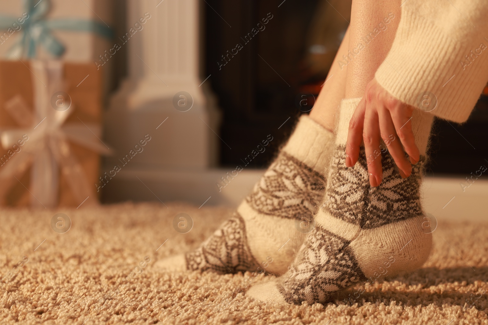 Photo of Woman in warm socks resting near fireplace at home, closeup. Space for text