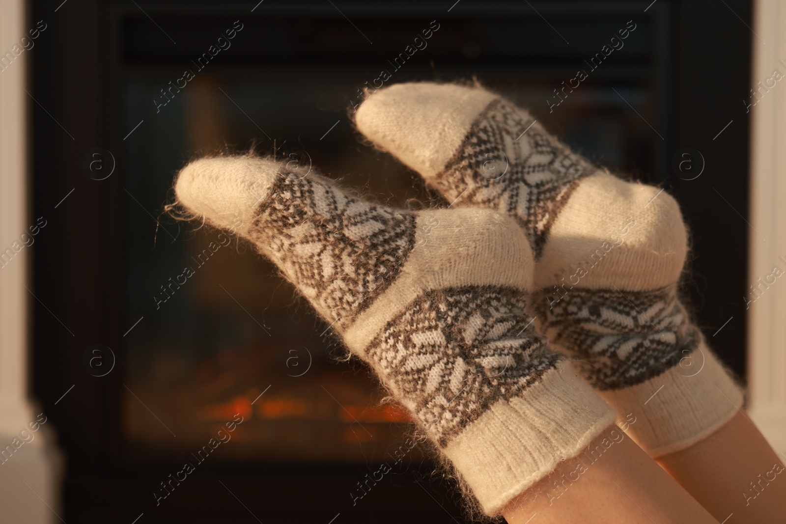 Photo of Woman in warm socks resting near fireplace at home, closeup