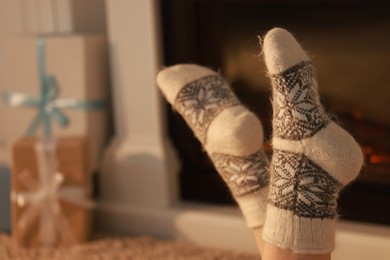 Woman in warm socks resting near fireplace at home, closeup