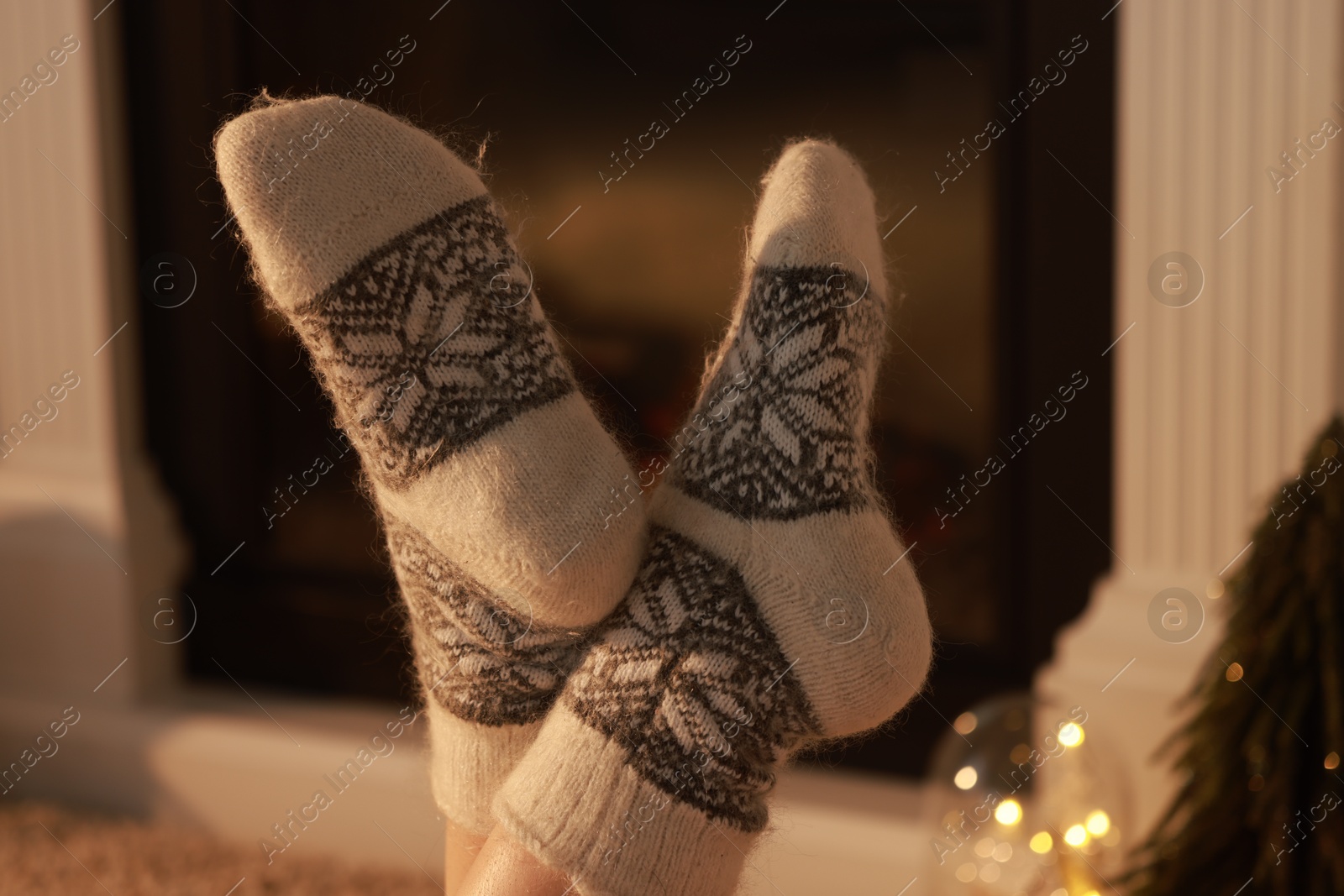 Photo of Woman in warm socks resting near fireplace at home, closeup