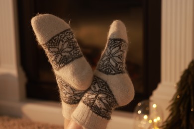 Woman in warm socks resting near fireplace at home, closeup