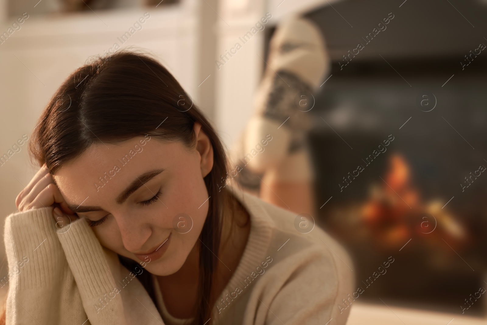 Photo of Woman in warm sweater resting near fireplace at home