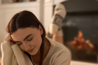 Woman in warm sweater resting near fireplace at home