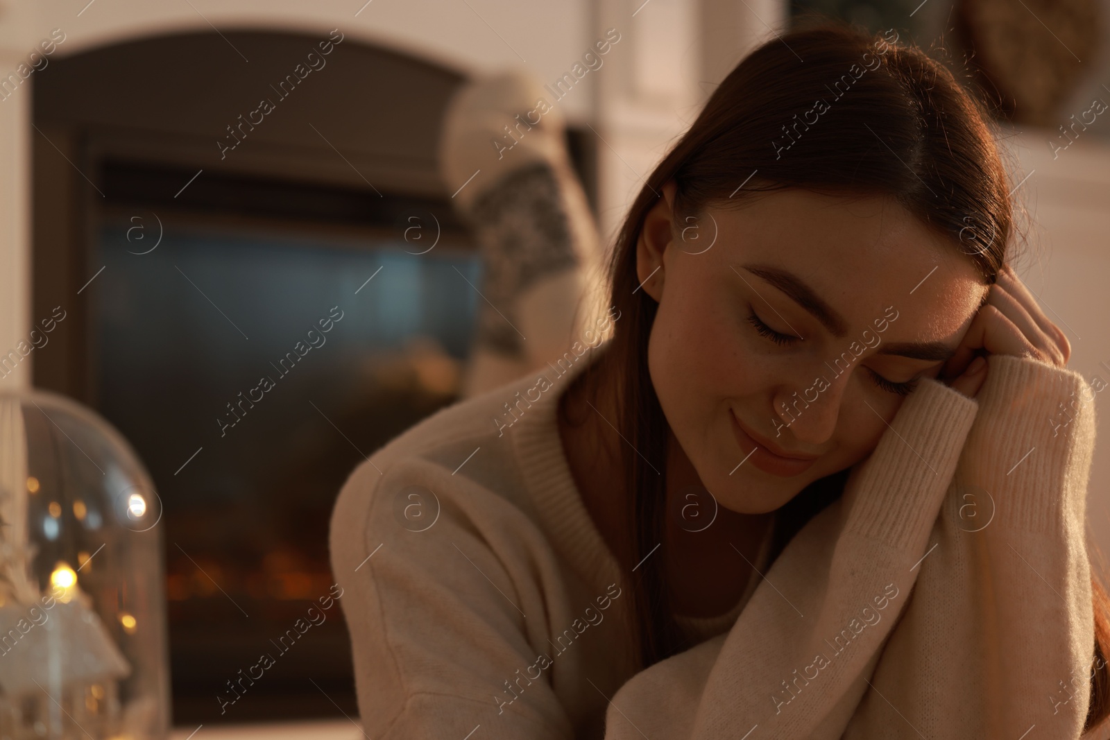 Photo of Woman in warm sweater resting near fireplace at home