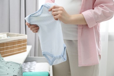 Photo of Pregnant woman with baby clothes at home, closeup