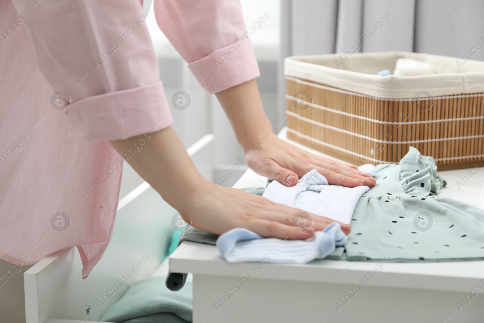 Photo of Woman folding baby clothes at home, closeup