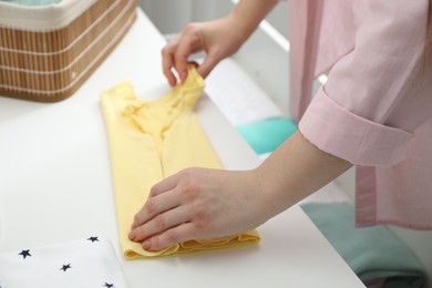 Photo of Woman folding baby clothes at home, closeup