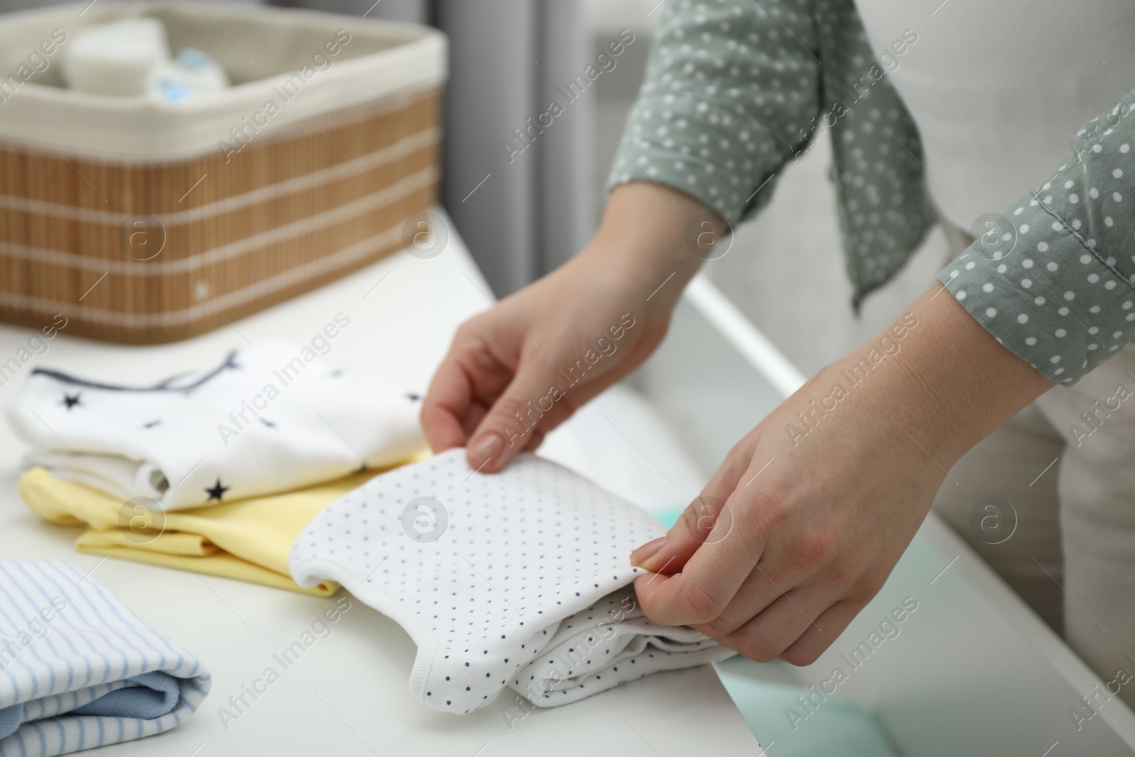 Photo of Woman folding baby clothes at home, closeup