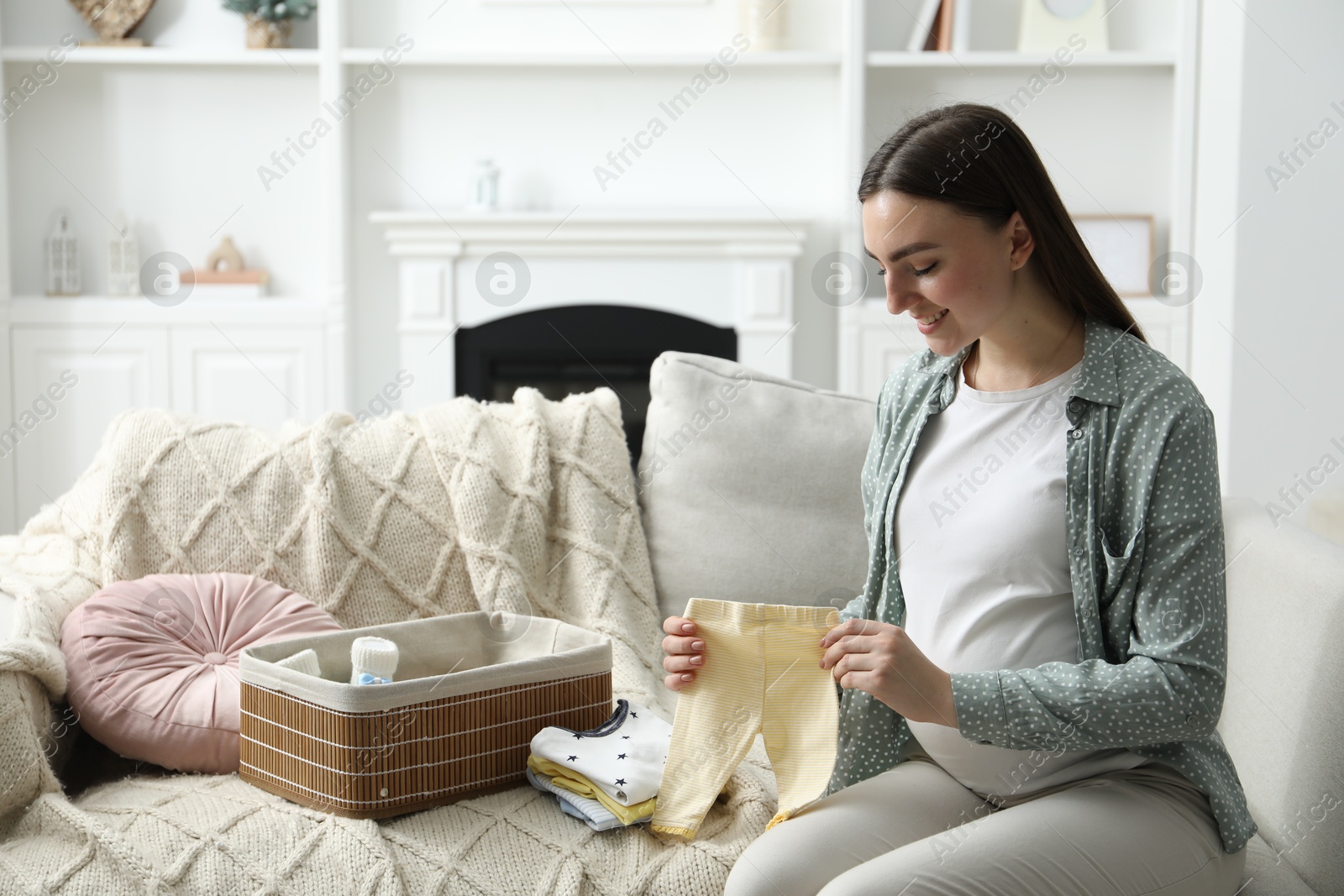 Photo of Pregnant woman with baby clothes on sofa at home