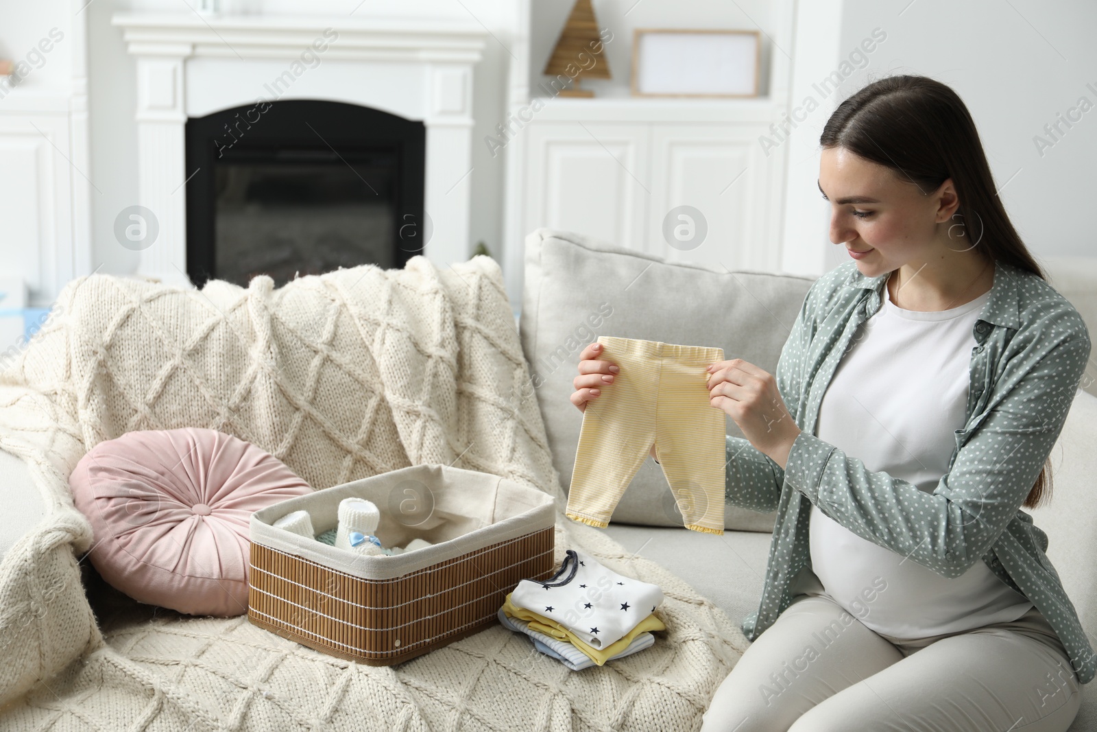 Photo of Pregnant woman with baby clothes on sofa at home