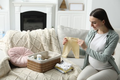 Photo of Pregnant woman with baby clothes on sofa at home