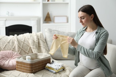 Photo of Pregnant woman with baby clothes on sofa at home