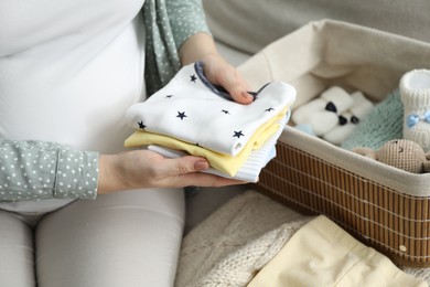 Photo of Pregnant woman with baby clothes on sofa at home, closeup