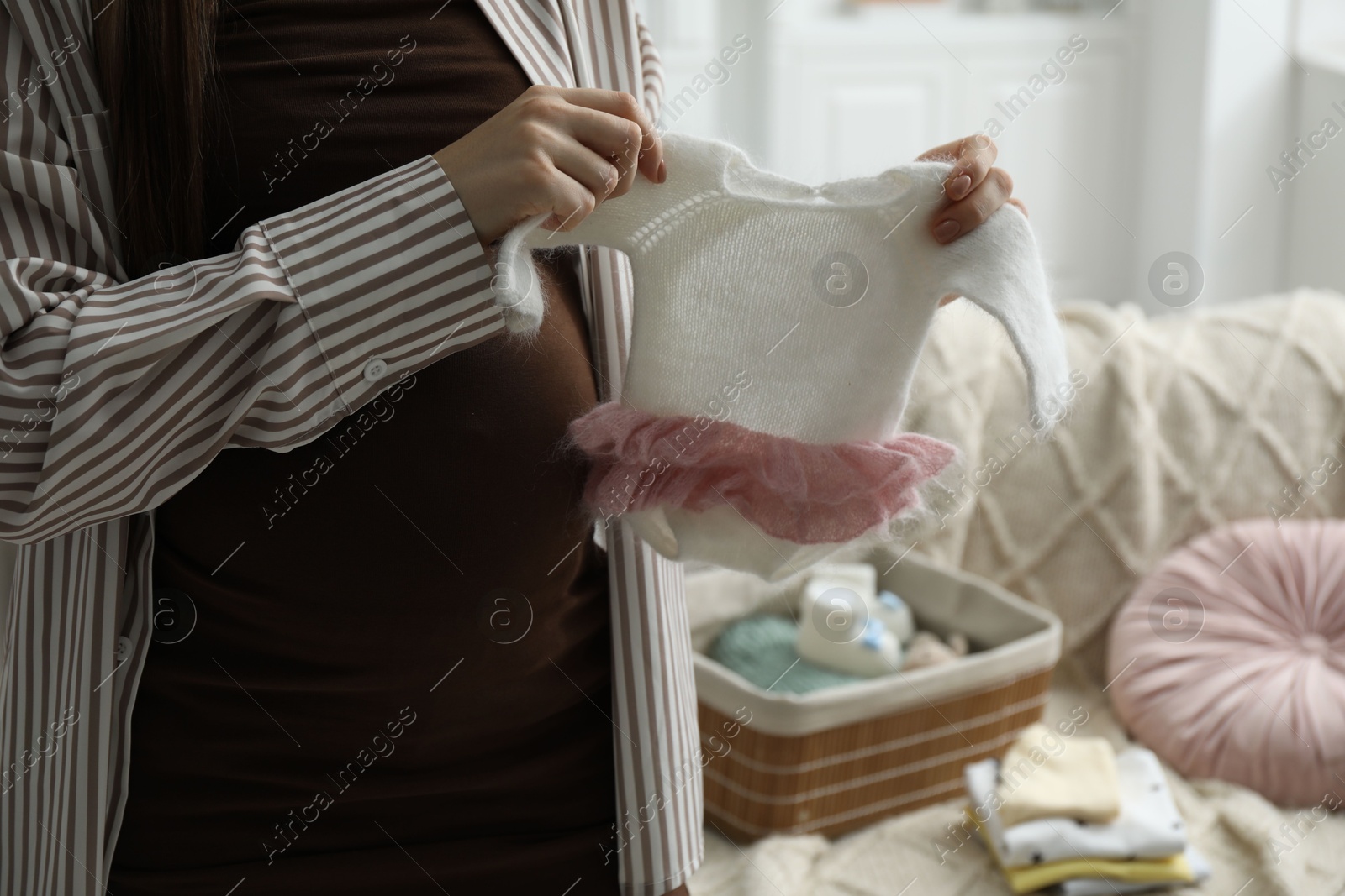 Photo of Pregnant woman with baby clothes at home, closeup