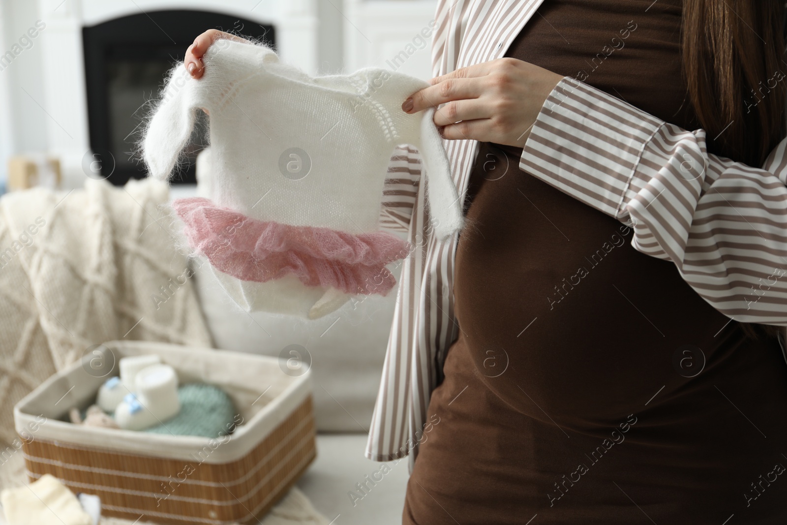 Photo of Pregnant woman with baby clothes at home, closeup