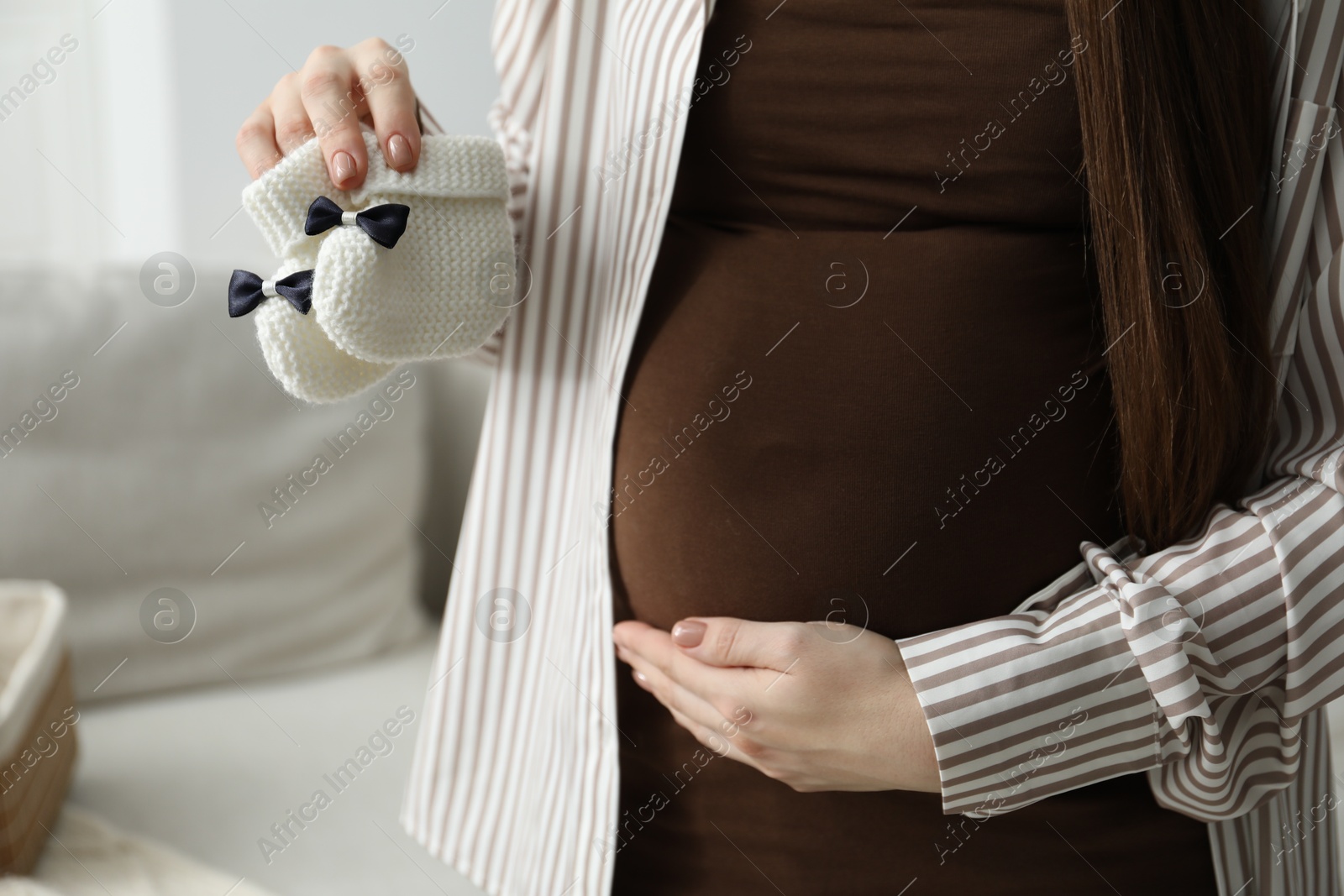 Photo of Pregnant woman with baby booties at home, closeup