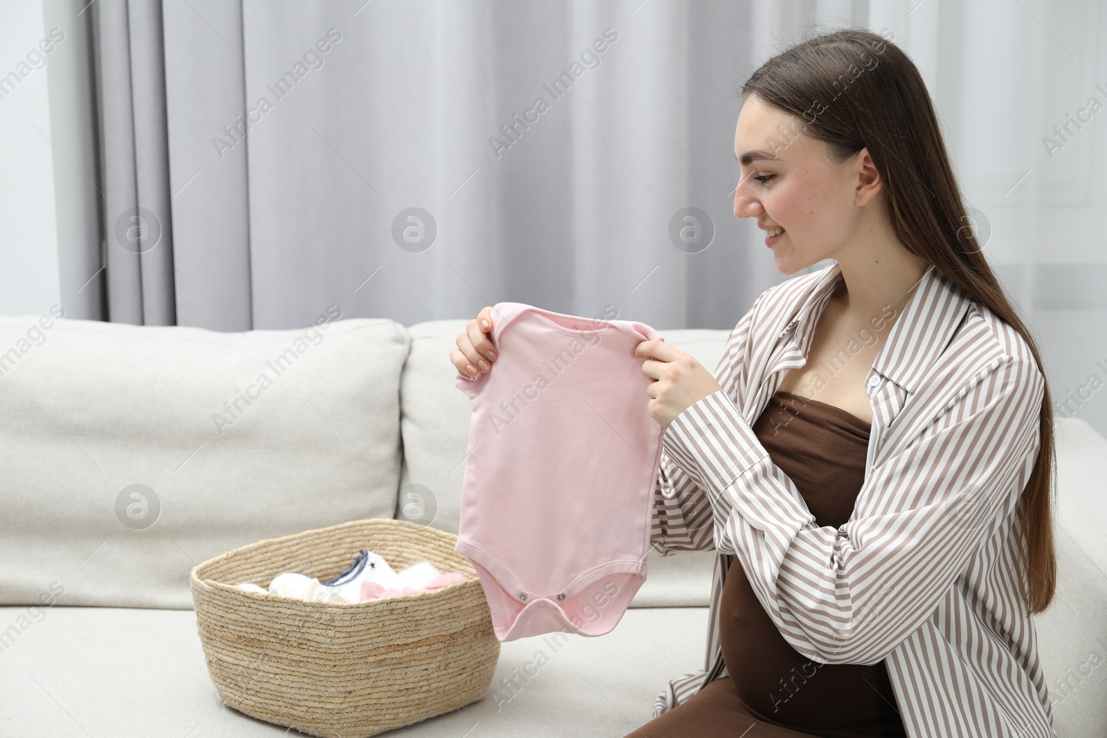 Photo of Pregnant woman with baby clothes on sofa at home