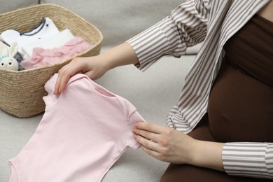 Photo of Pregnant woman with baby clothes on sofa at home, closeup