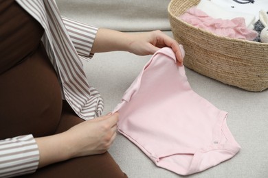 Photo of Pregnant woman with baby clothes on sofa at home, closeup