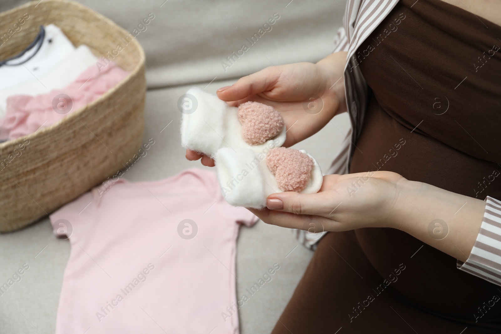 Photo of Pregnant woman with baby socks on sofa at home, closeup