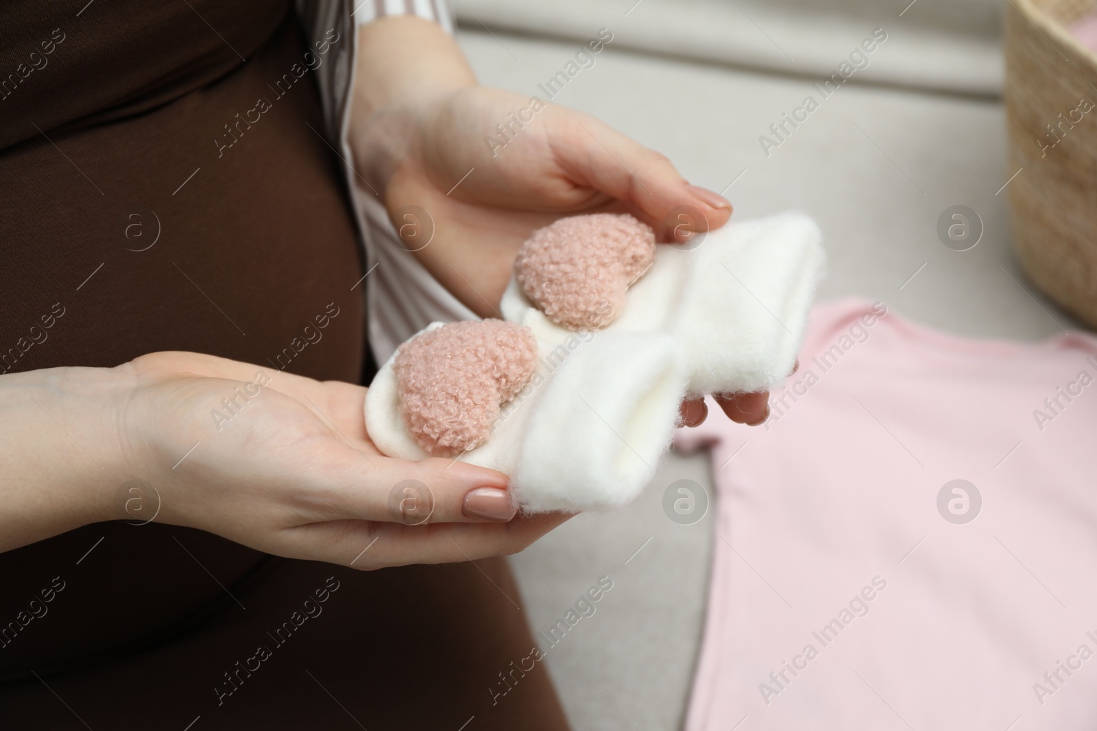 Photo of Pregnant woman with baby socks on sofa at home, closeup