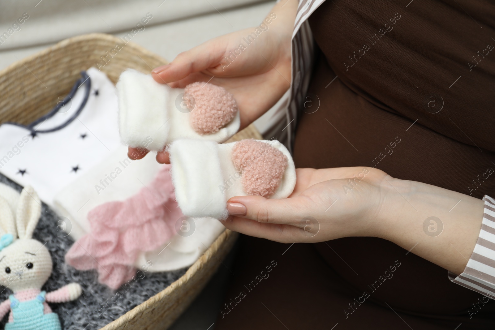 Photo of Pregnant woman with baby socks on sofa at home, closeup