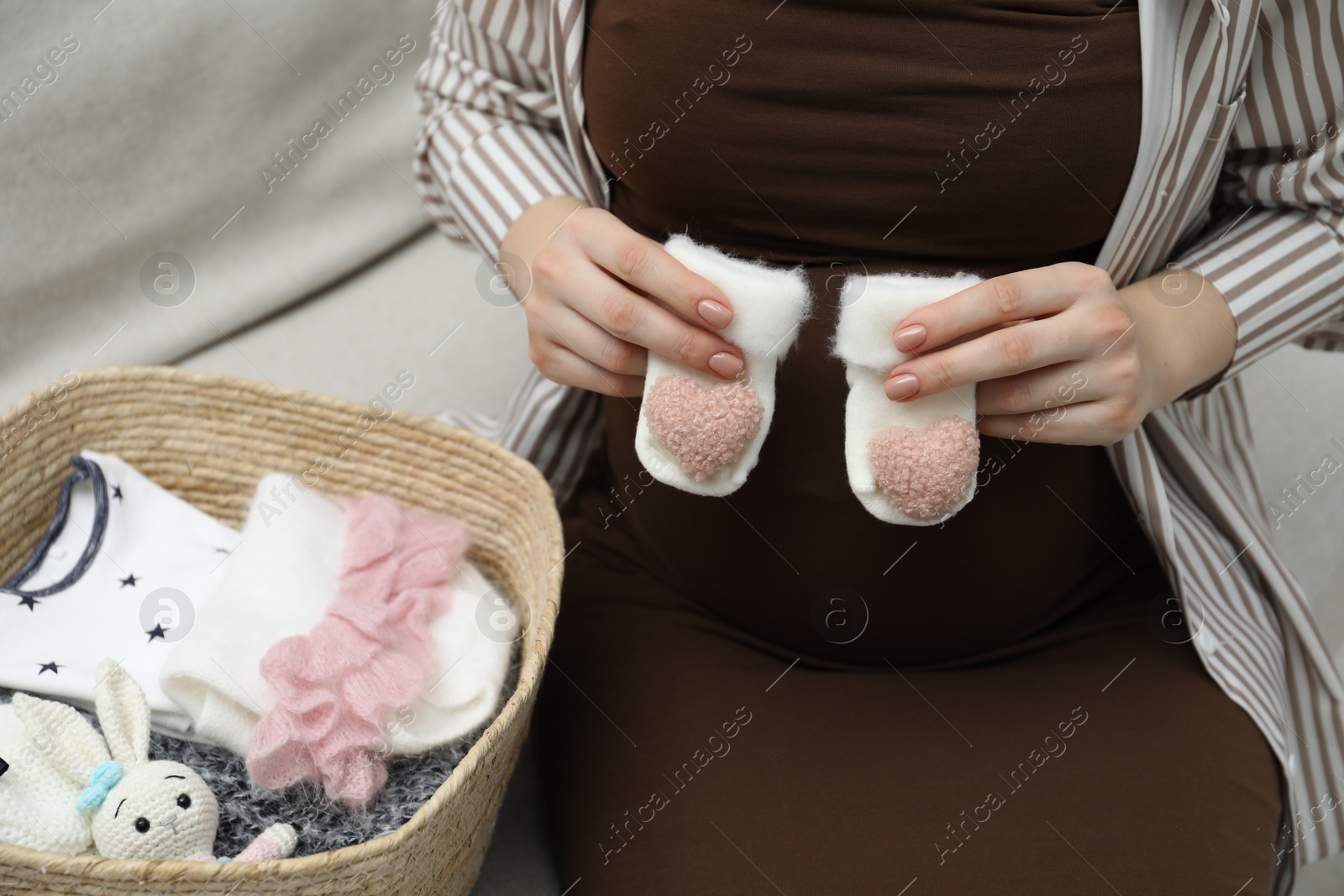 Photo of Pregnant woman with baby socks on sofa at home, closeup