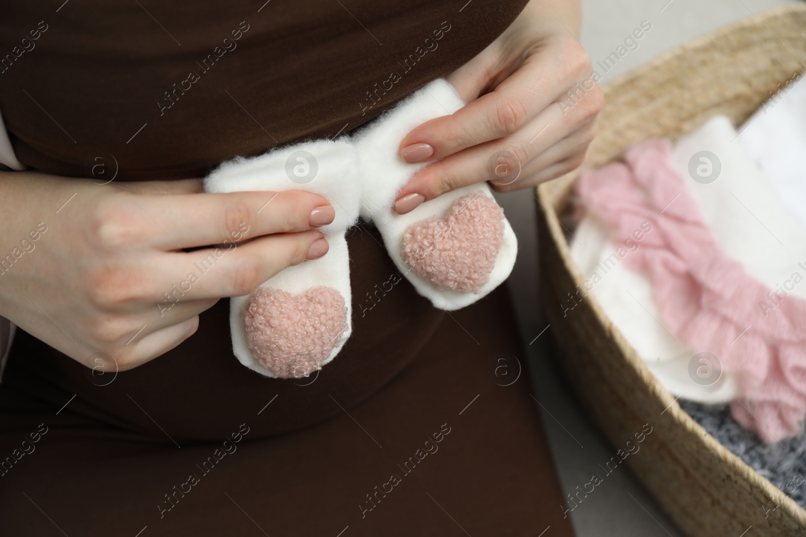 Photo of Pregnant woman with baby socks on sofa at home, closeup