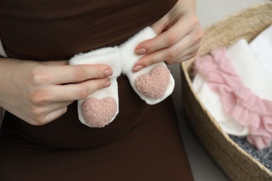 Photo of Pregnant woman with baby socks on sofa at home, closeup