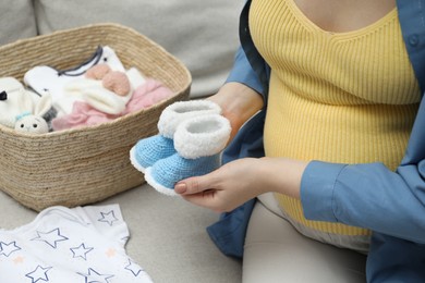 Photo of Pregnant woman with baby booties on sofa at home, closeup