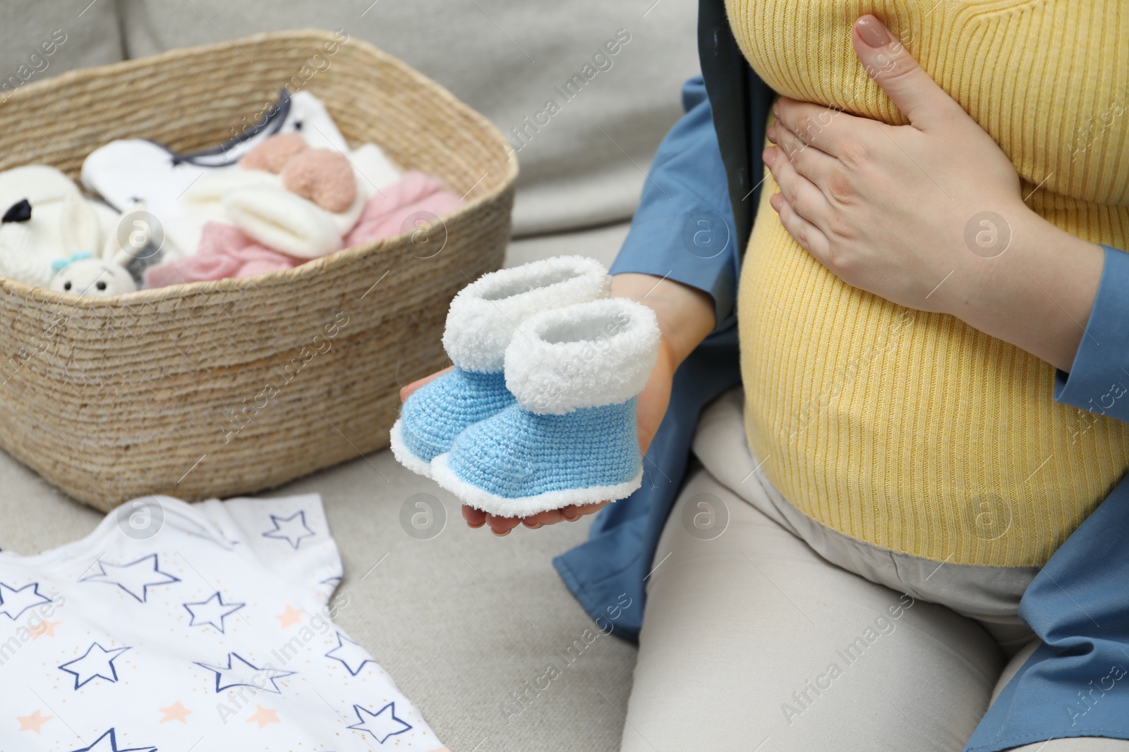 Photo of Pregnant woman with baby booties on sofa at home, closeup