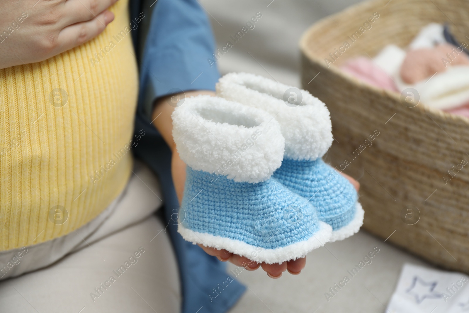 Photo of Pregnant woman with baby booties on sofa at home, closeup