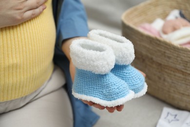 Photo of Pregnant woman with baby booties on sofa at home, closeup