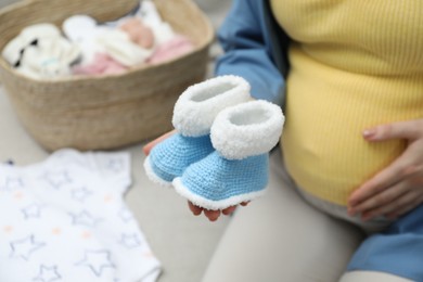 Photo of Pregnant woman with baby booties on sofa at home, closeup