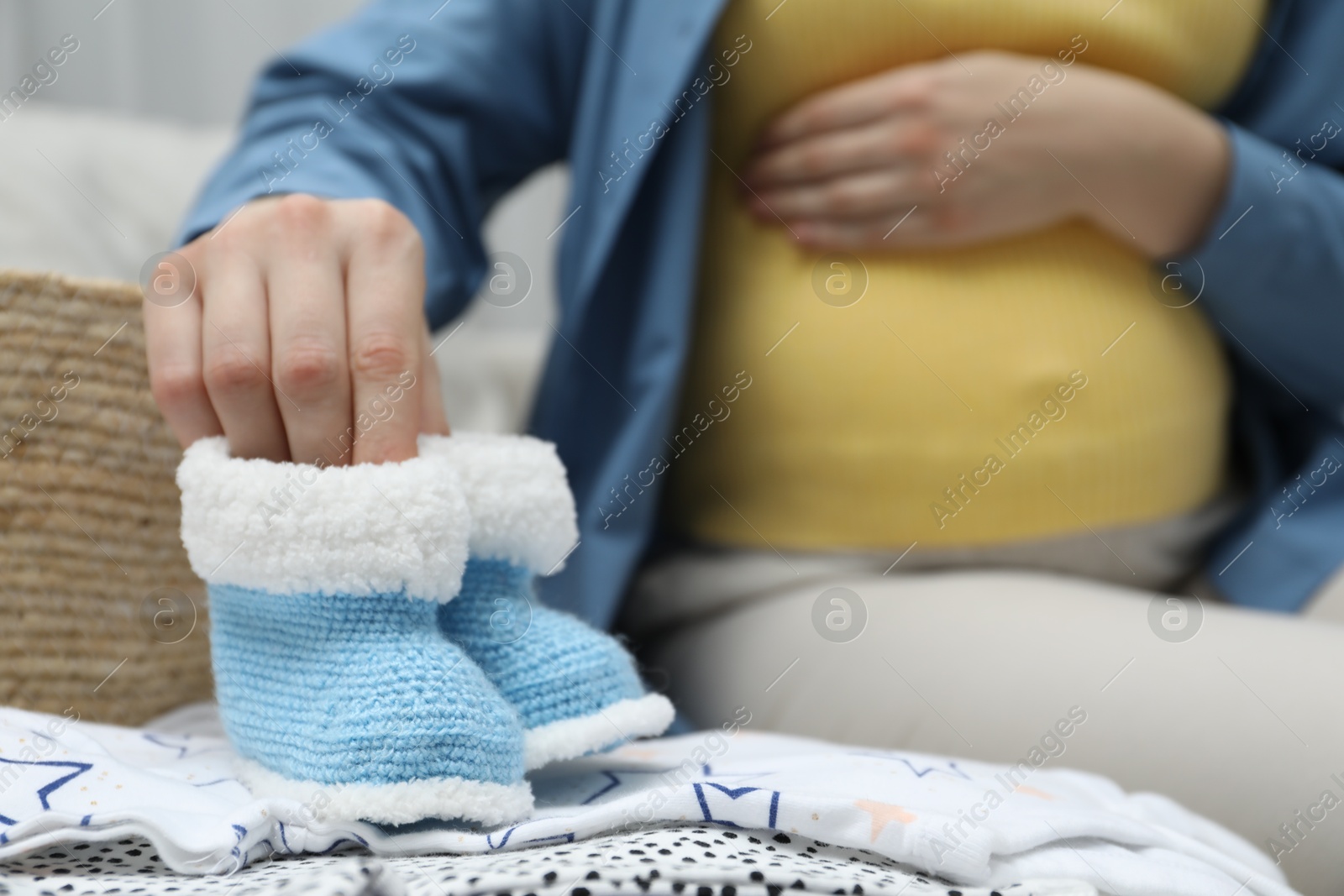 Photo of Pregnant woman with baby booties on sofa at home, closeup