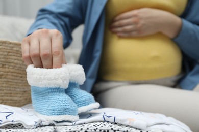 Photo of Pregnant woman with baby booties on sofa at home, closeup