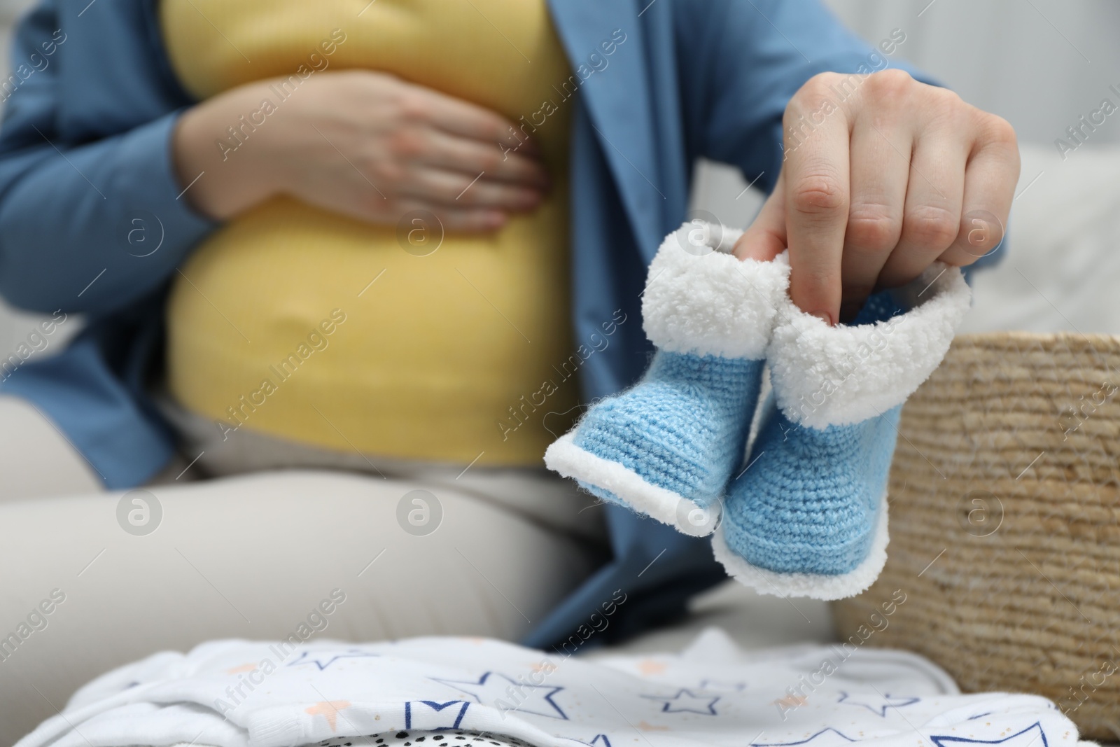 Photo of Pregnant woman with baby booties on sofa at home, closeup