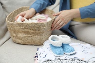 Photo of Pregnant woman with baby clothes on sofa at home, closeup